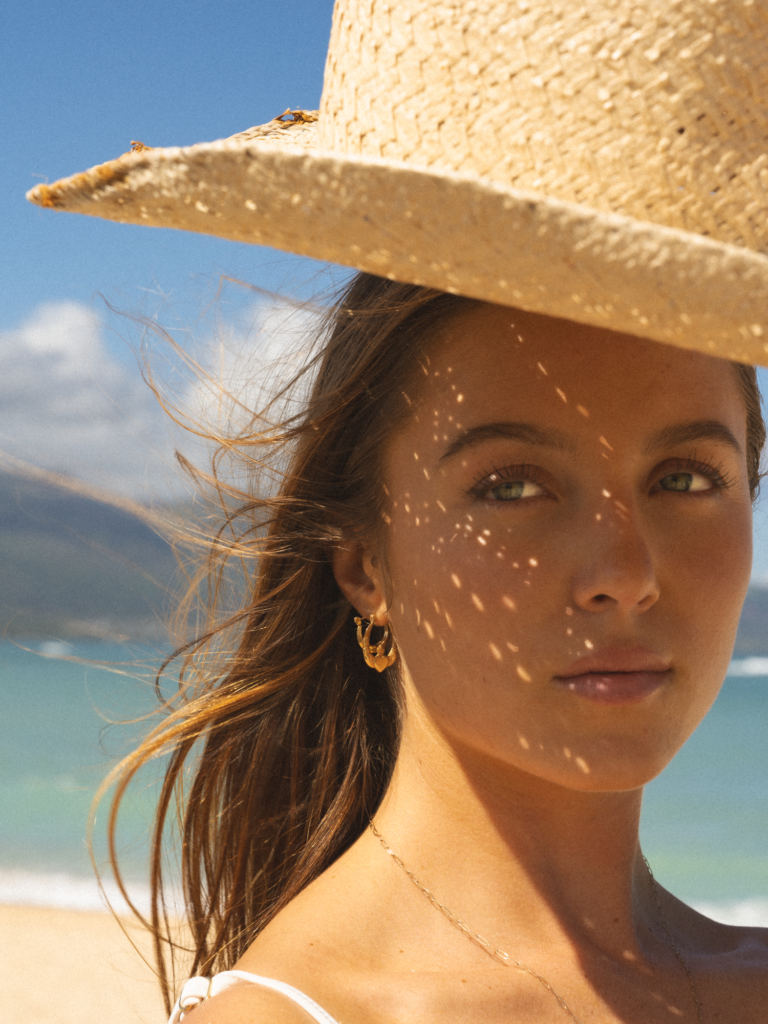 girl staring out into the sun with hues of light shining through her hat on a beach in maui