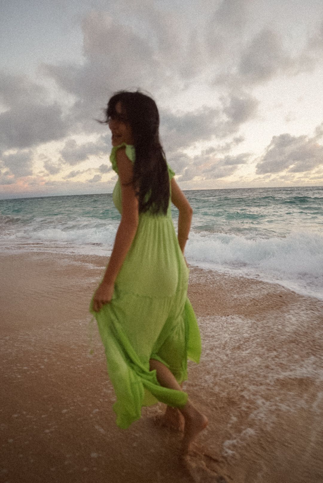 girl running the beach in a green dress watching the sunrise at a beach in kauai