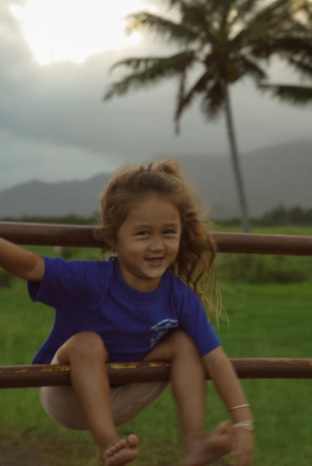 little girl plying on a fence near a girls of grass in Kauai