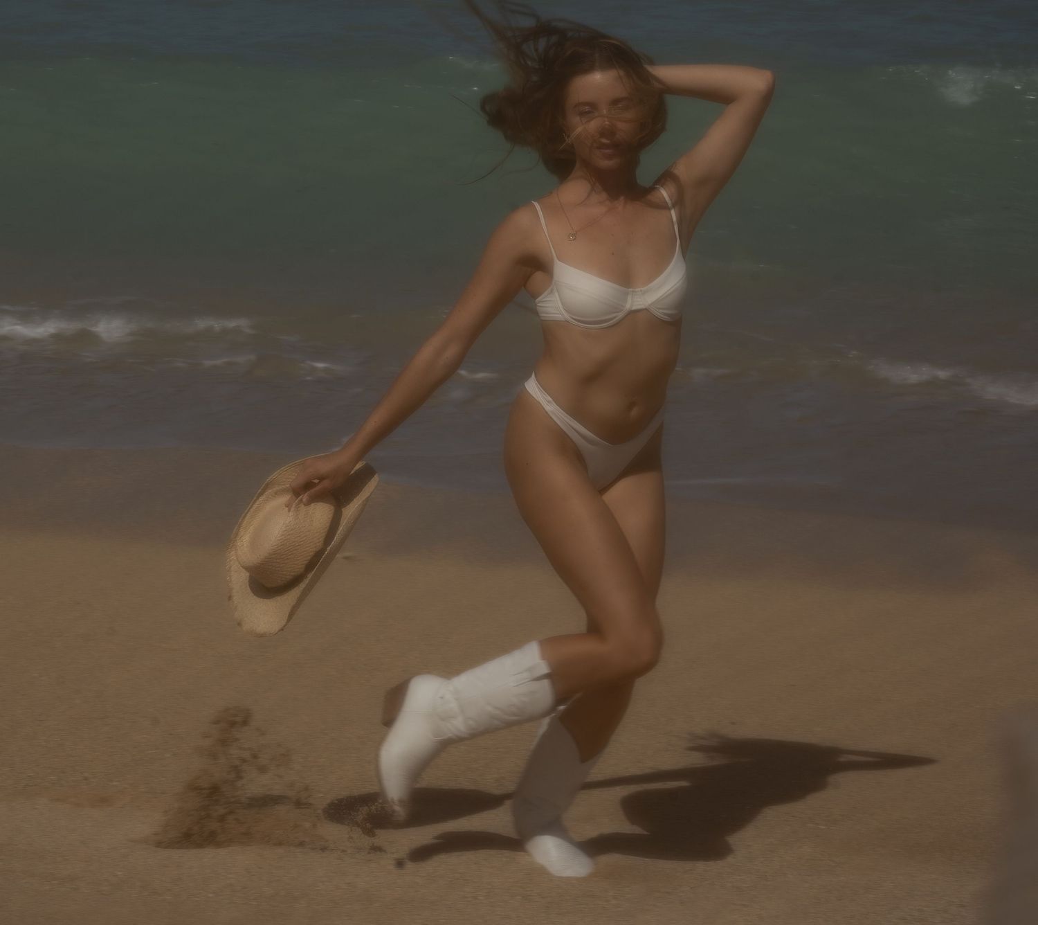 girl running the beach with her hat in her hand, on a sandy beach with boots