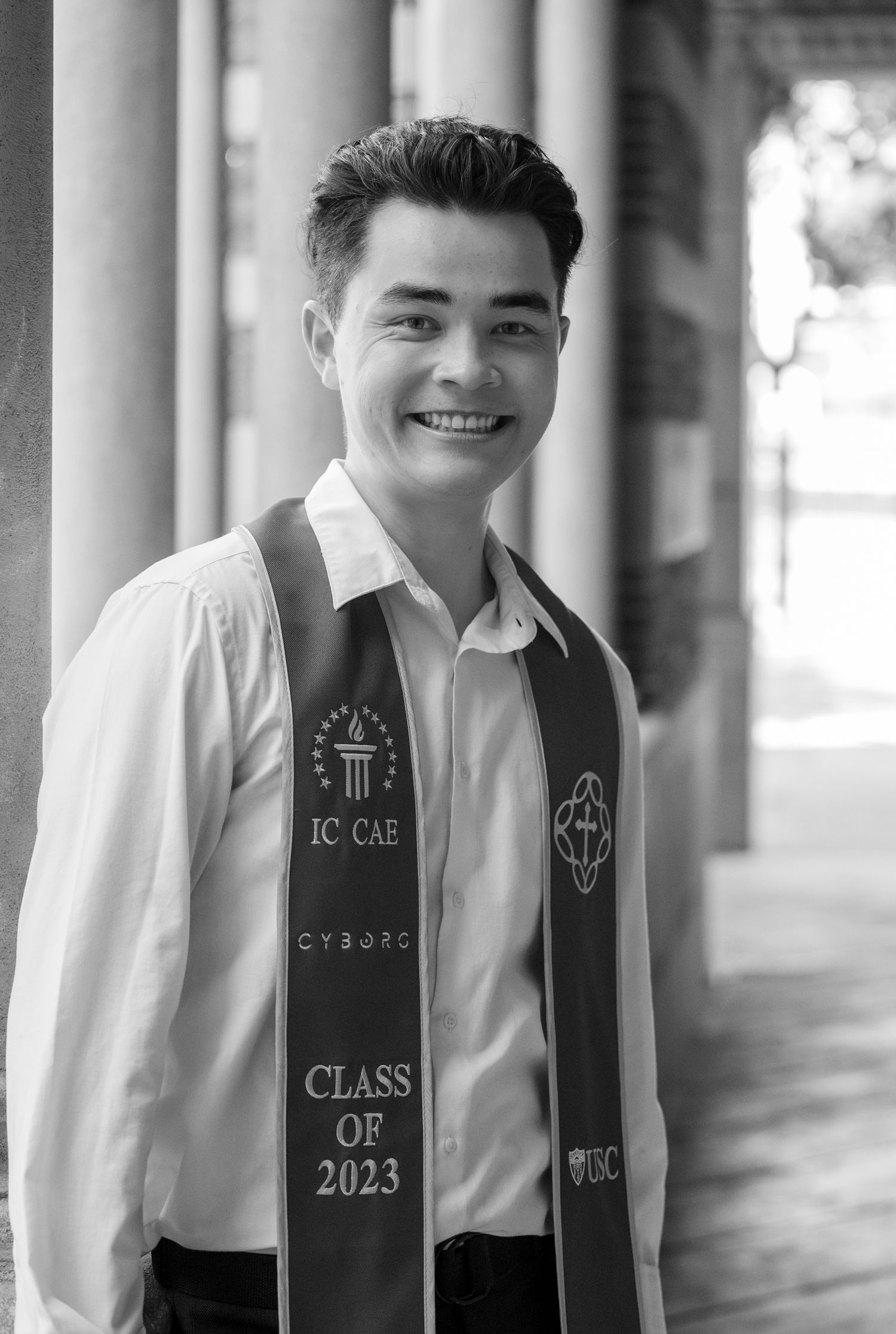 Graduate in white shirt and graduation stole from Class of 2023 poses in black and white portrait.