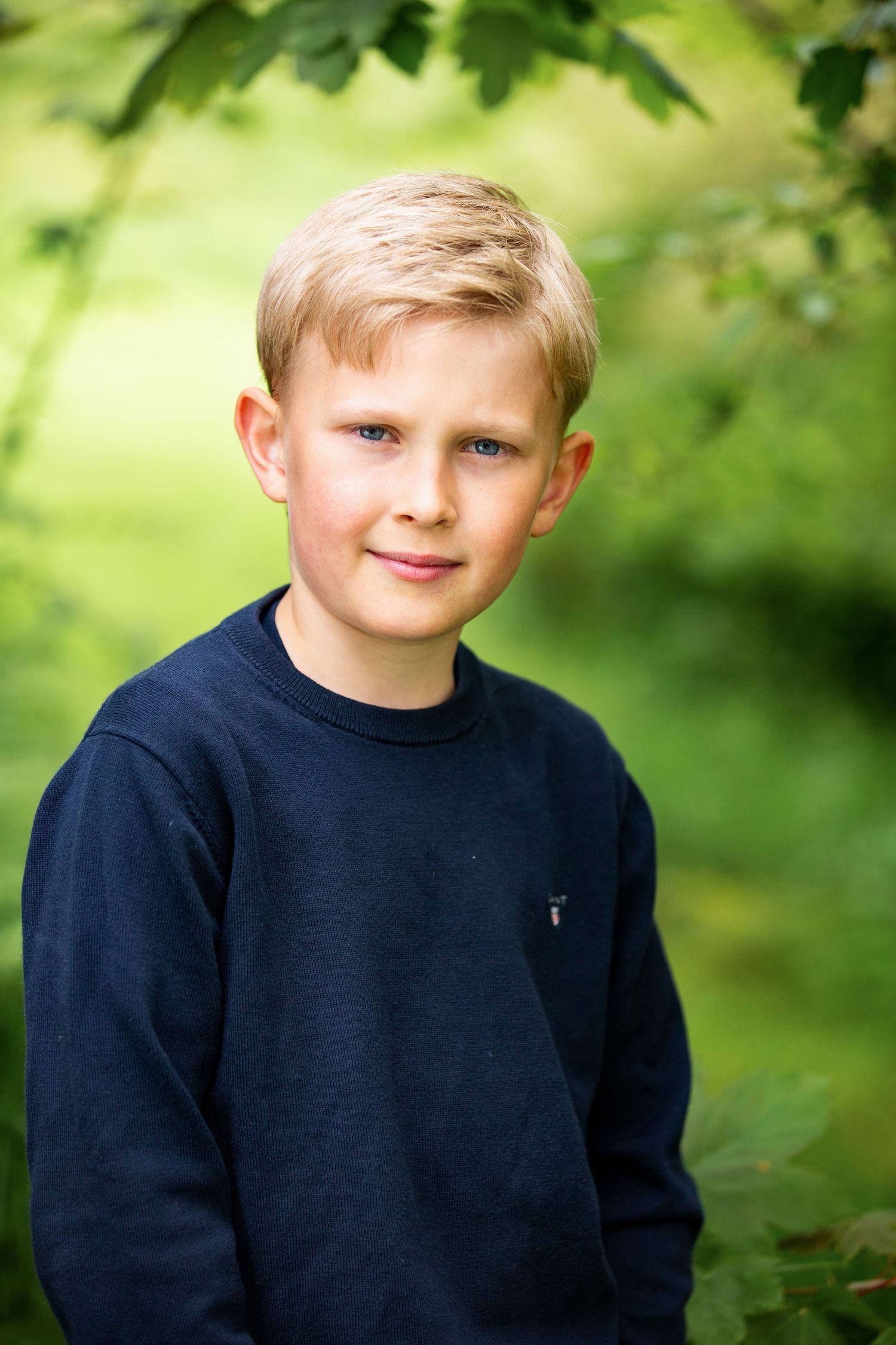 Youth in navy sweater photographed outdoors with green foliage background.