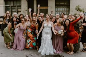 Large bridal party in mix of pink, floral and colorful dresses posing together outdoors.