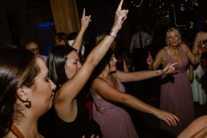 Wedding reception guests dancing with arms raised on dark dance floor.