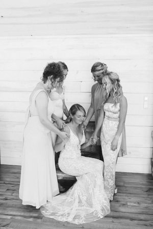 Black and white photo of wedding dress preparations with attendants helping.