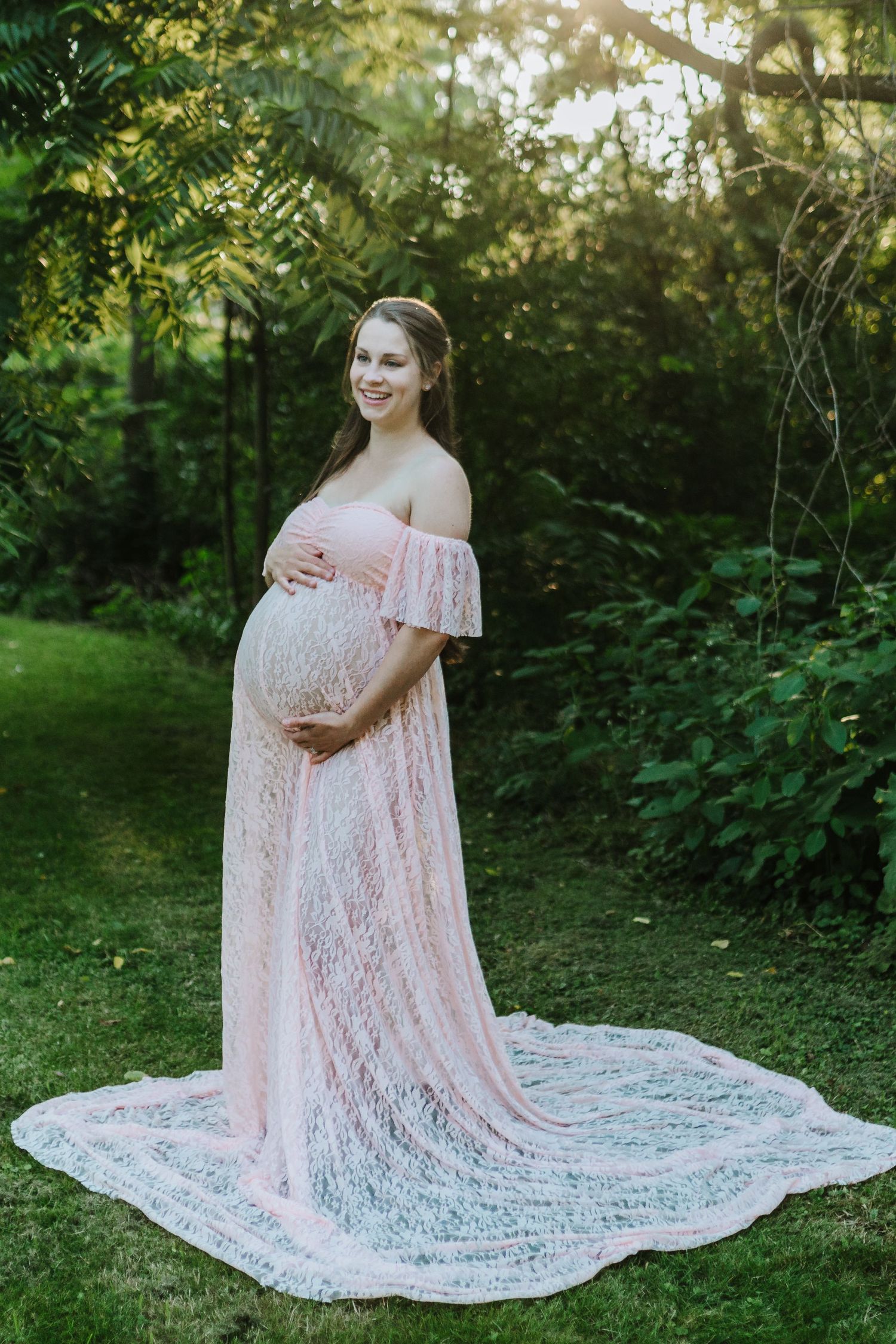 Ethereal maternity photograph in pink lace dress with train in woodland setting.