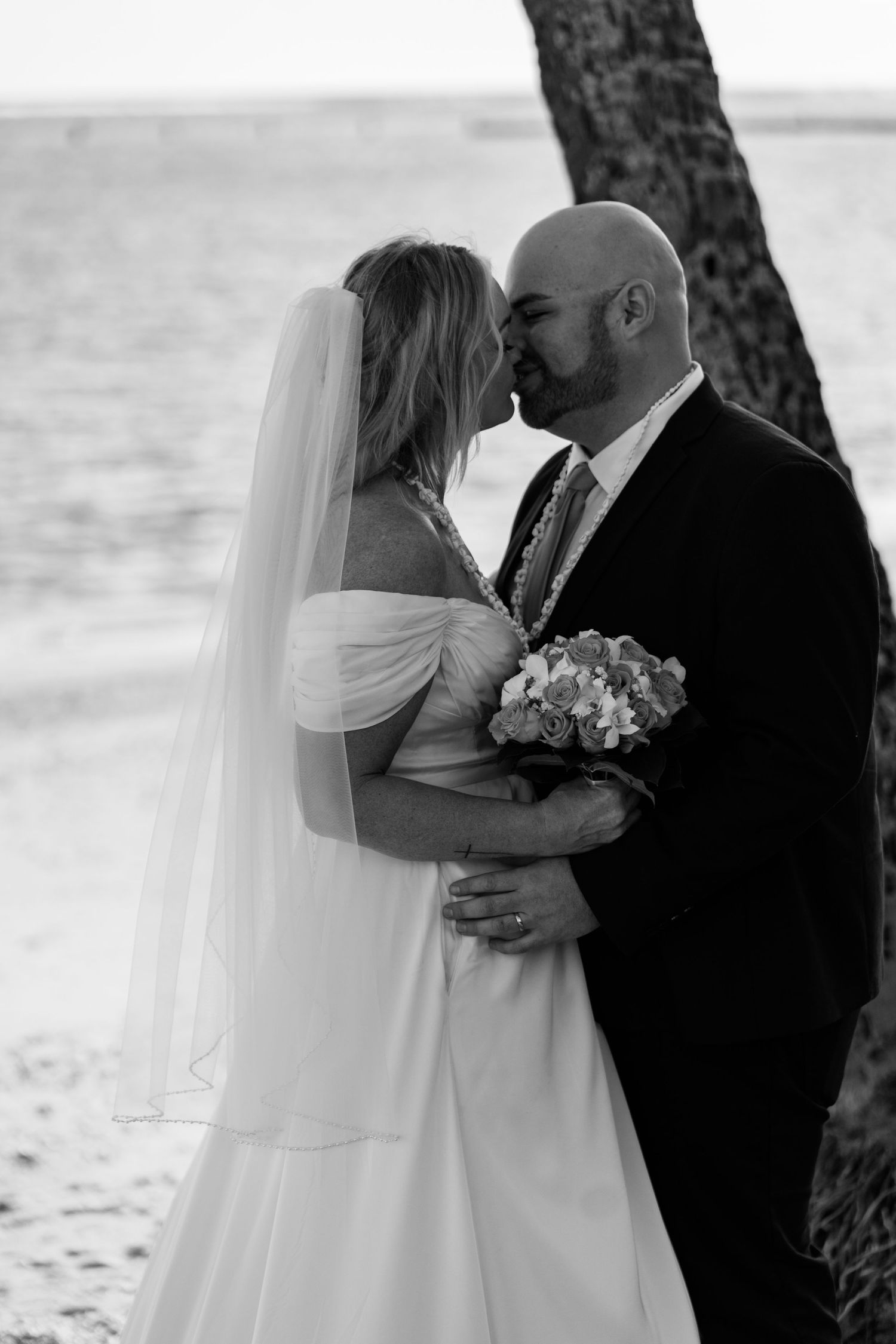 A black and white intimate portrait of newlyweds embracing on a beach.