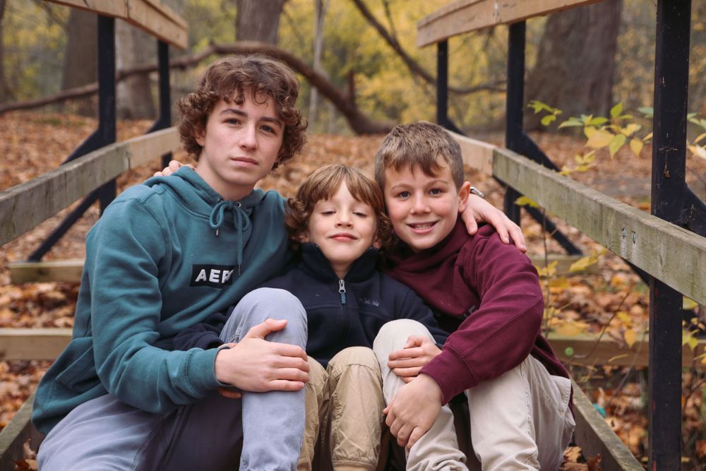 Three boys sitting on a wooden bridge in the fall.