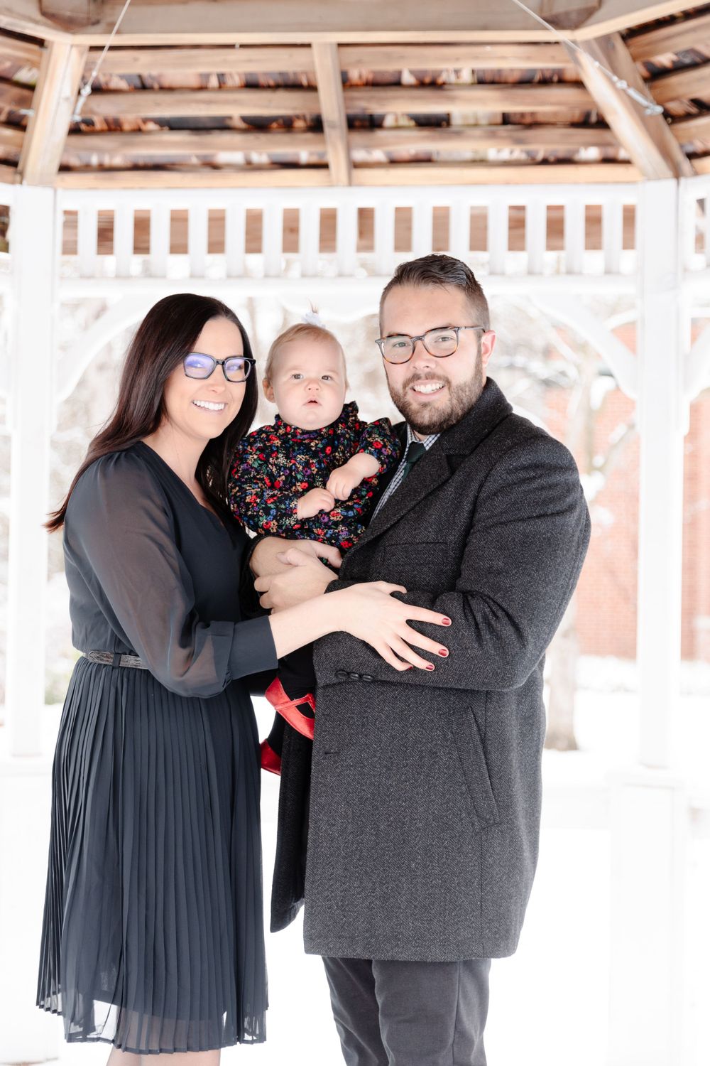 A man and woman holding a baby in front of a gazebo.