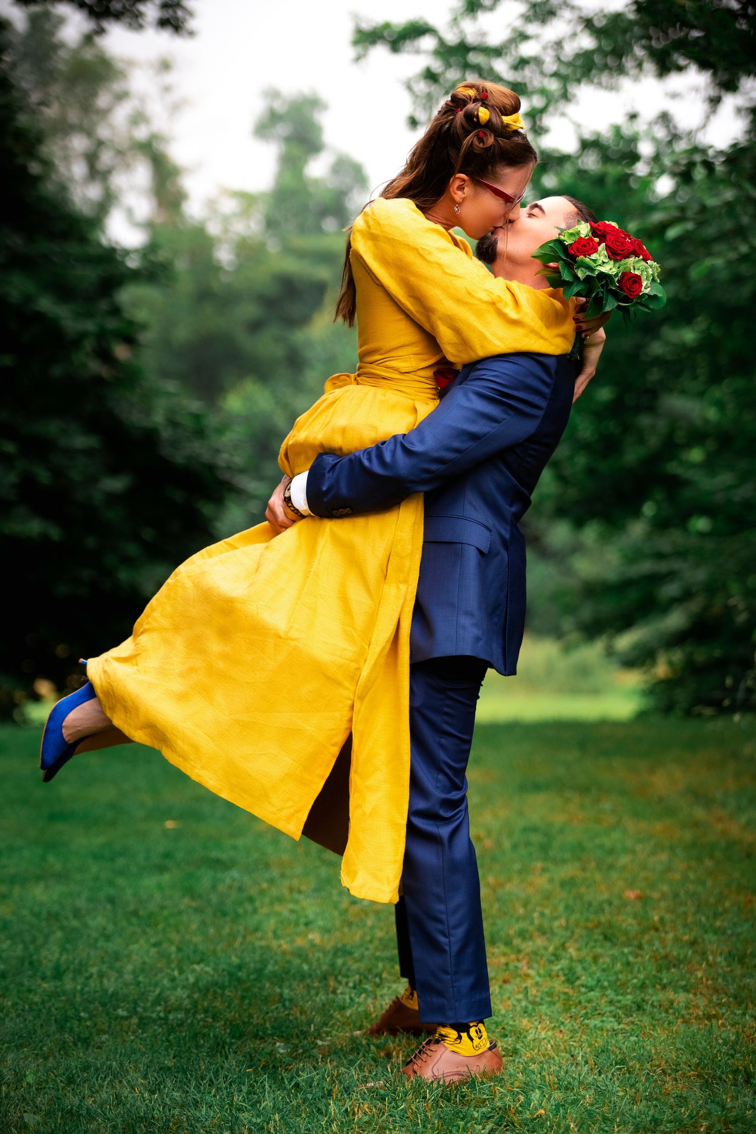 A couple embracing outdoors, with one wearing a vibrant yellow coat and holding red roses.