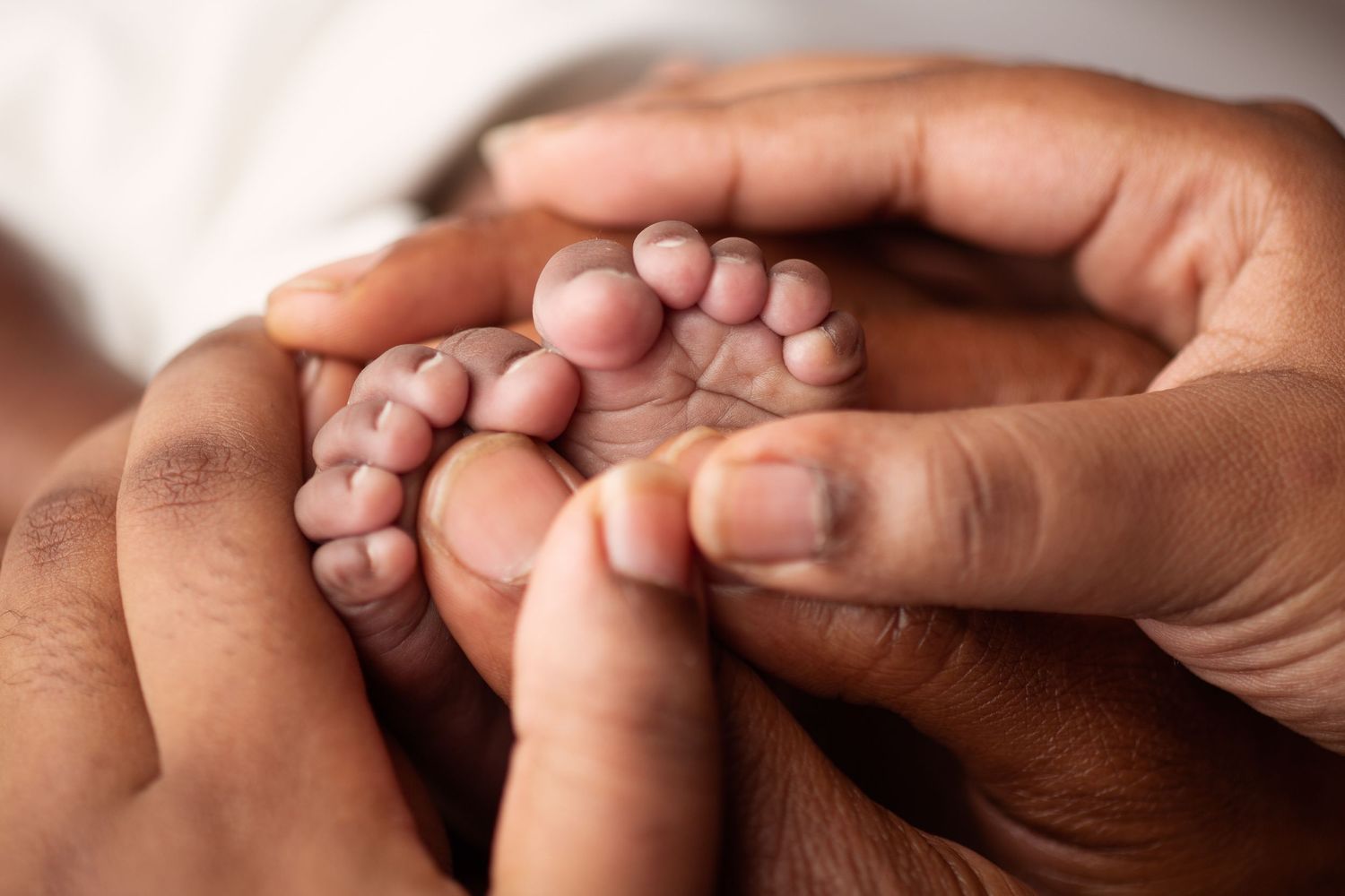 Adult hands gently cradling tiny newborn baby feet in a close-up tender moment.