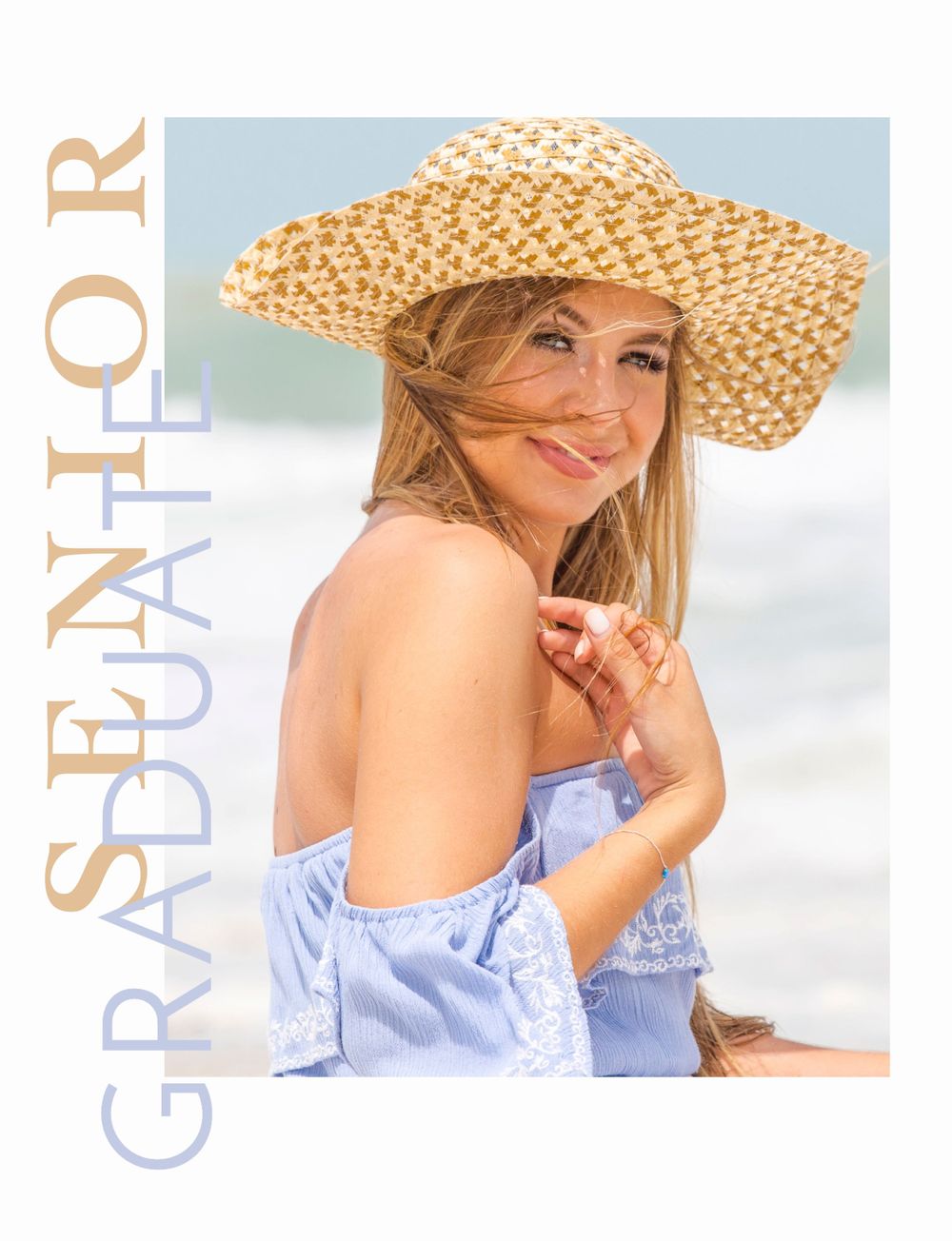 A smiling senior graduate poses on the beach wearing a straw hat and blue off-shoulder top.