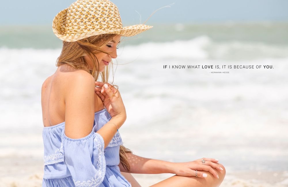A young woman in a blue top and straw hat sits on the beach with a romantic quote overlay.