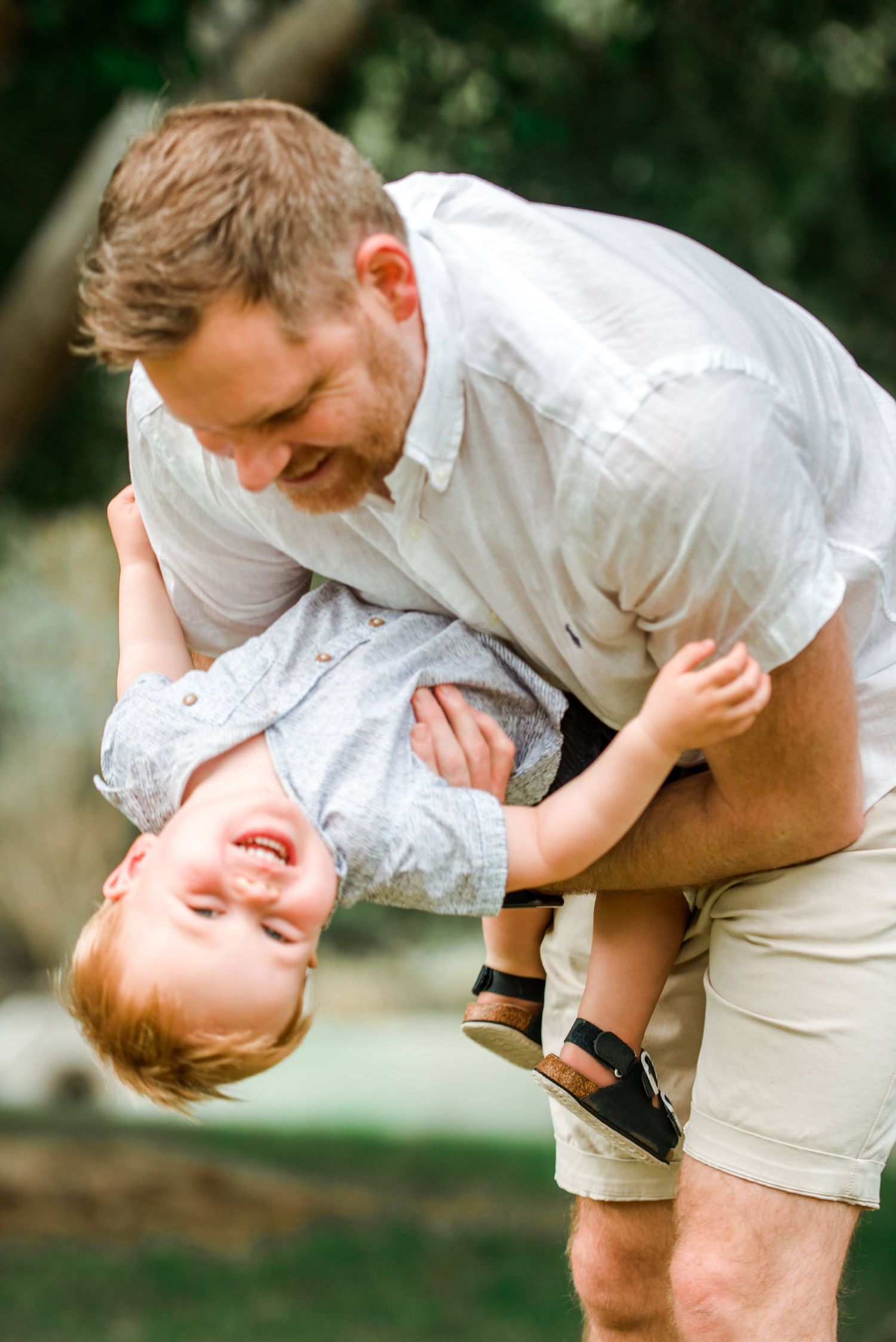 Parent playfully holding child upside down during fun outdoor portrait session.