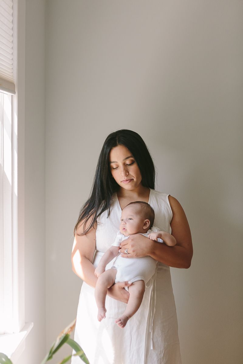 woman in white dress looking at her newborn child on a simple white background photo by Paula Ortiz NY Family Photograph