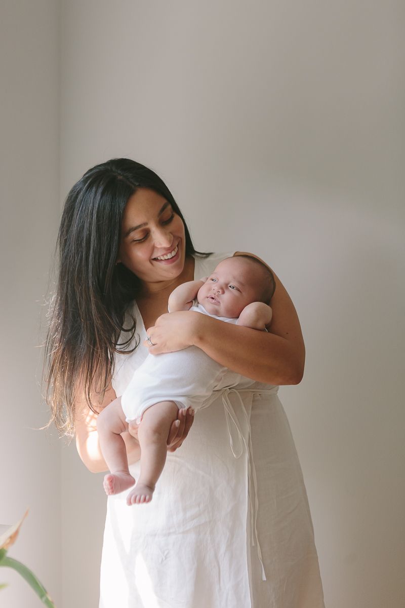 a mother smiles at her newborn stretching child in a candid moment by NYC Family Photographer Paula Ortiz