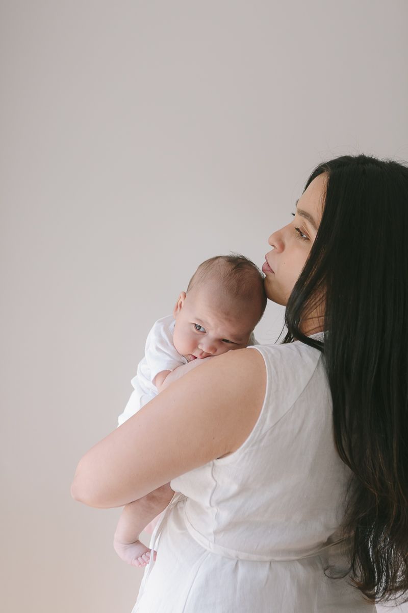 a profile view of a mother holding her newborn child against a plain white background during a newborn session in Queens