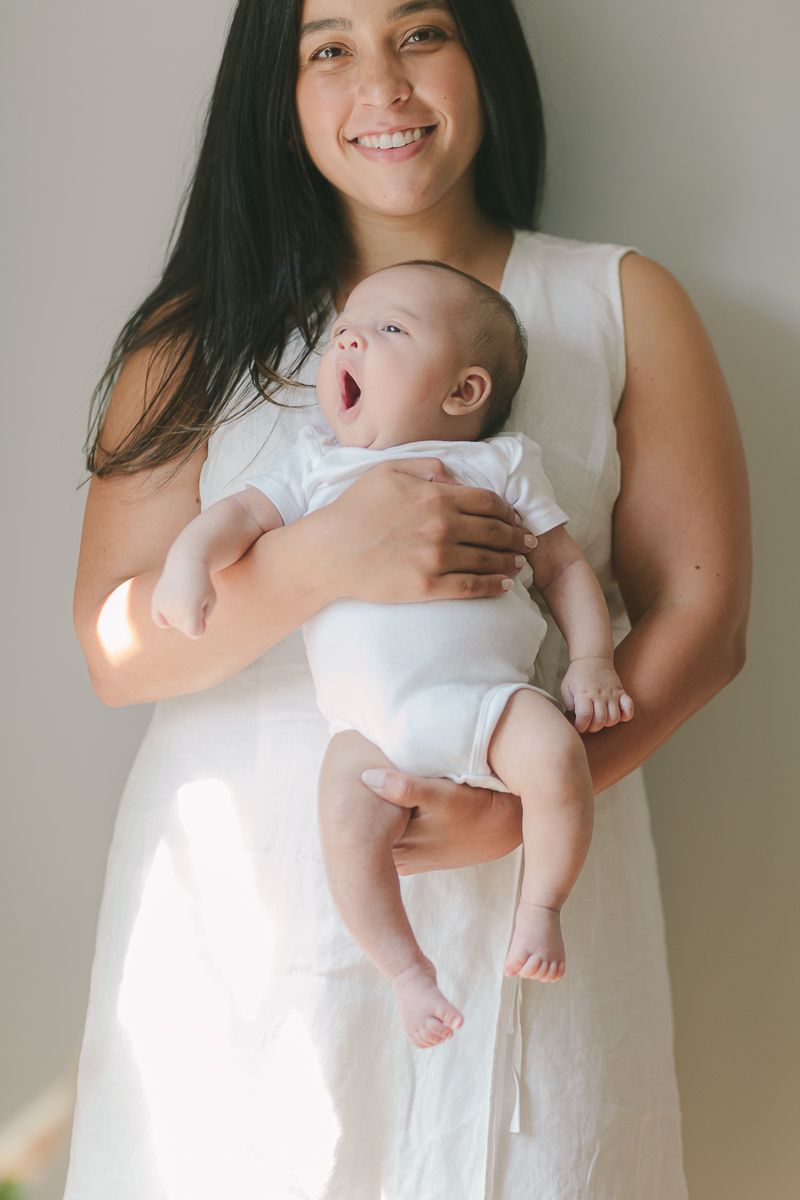 a candid moment of a newborn baby yawning while being held by her mother with beautiful light photo by Paula Ortiz NYC