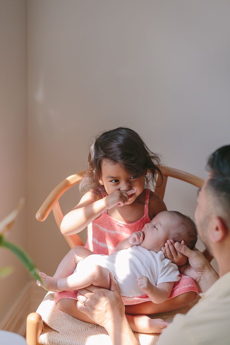 a funny candid moment of an toddler girl covering her nose with her finger while holding her newborn sister NYC