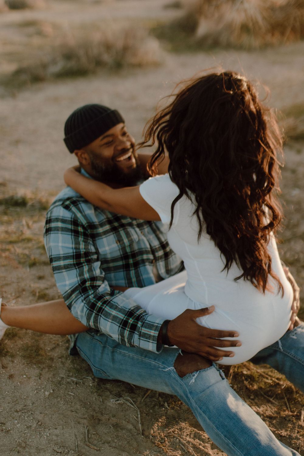 A couple shares a tender moment together outdoors, with one wearing a plaid flannel shirt and the other in white.