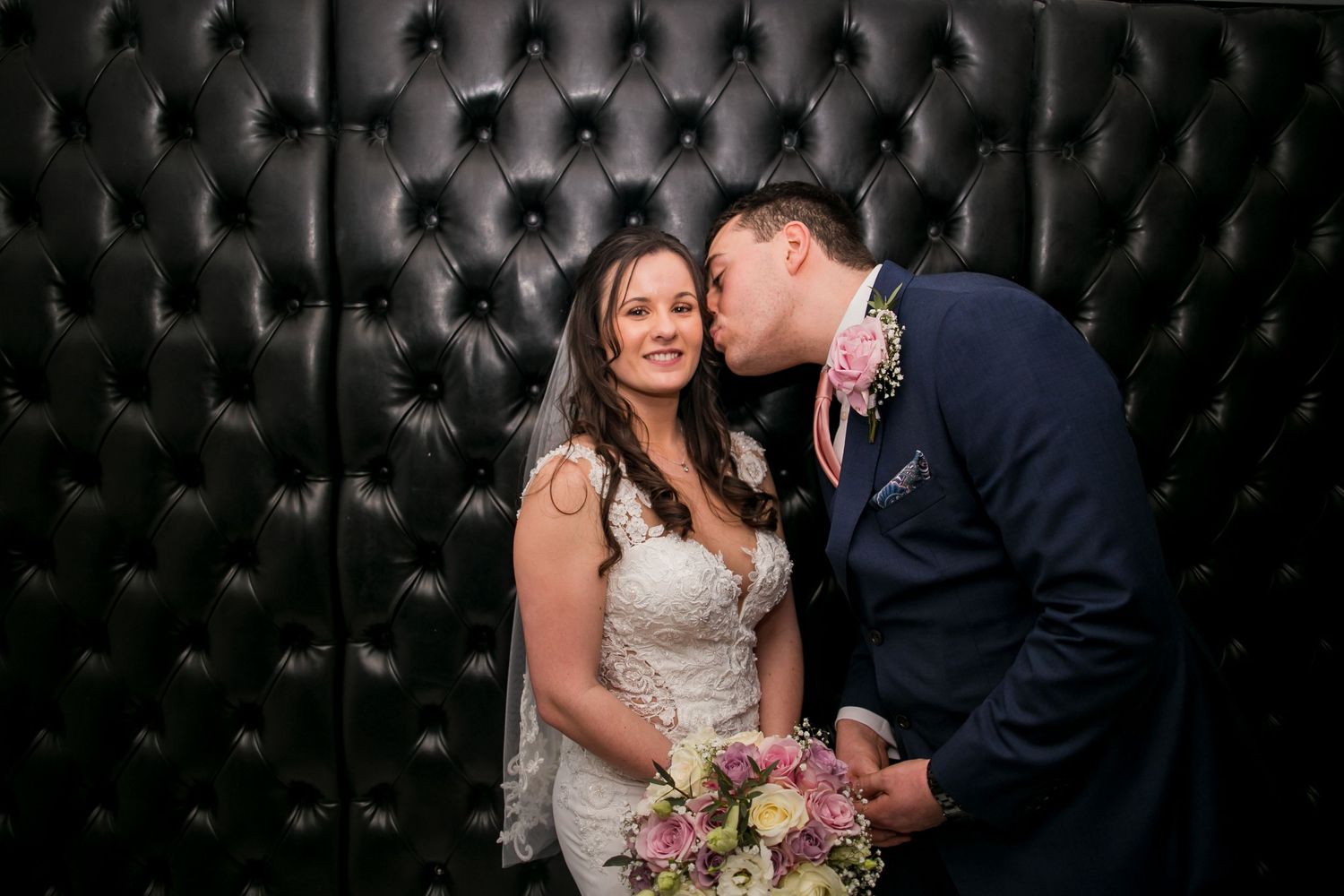 Romantic couple poses against an elegant black tufted backdrop during their wedding celebration.