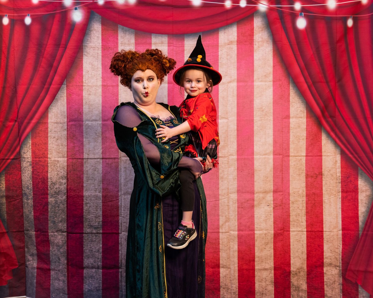 Festive Halloween scene with red and white striped circus backdrop and elegant vintage-inspired costume styling.
