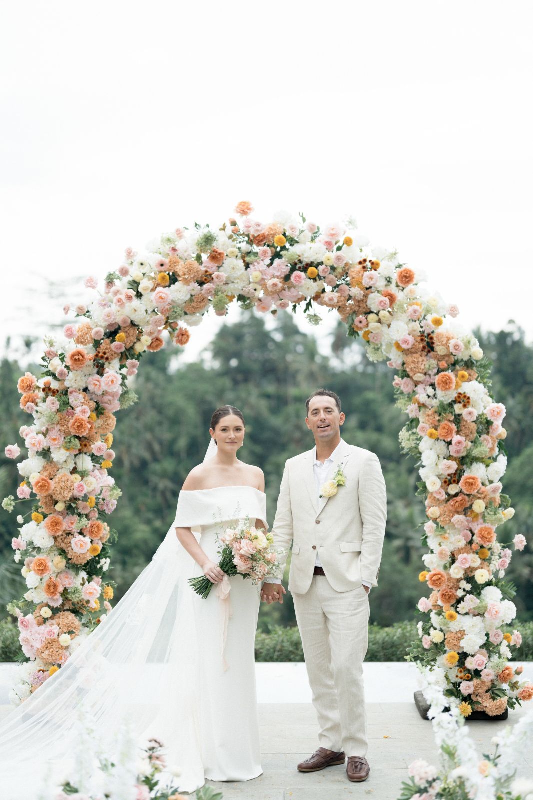 A beautiful floral arch with peach and white roses creates an elegant outdoor wedding ceremony backdrop.