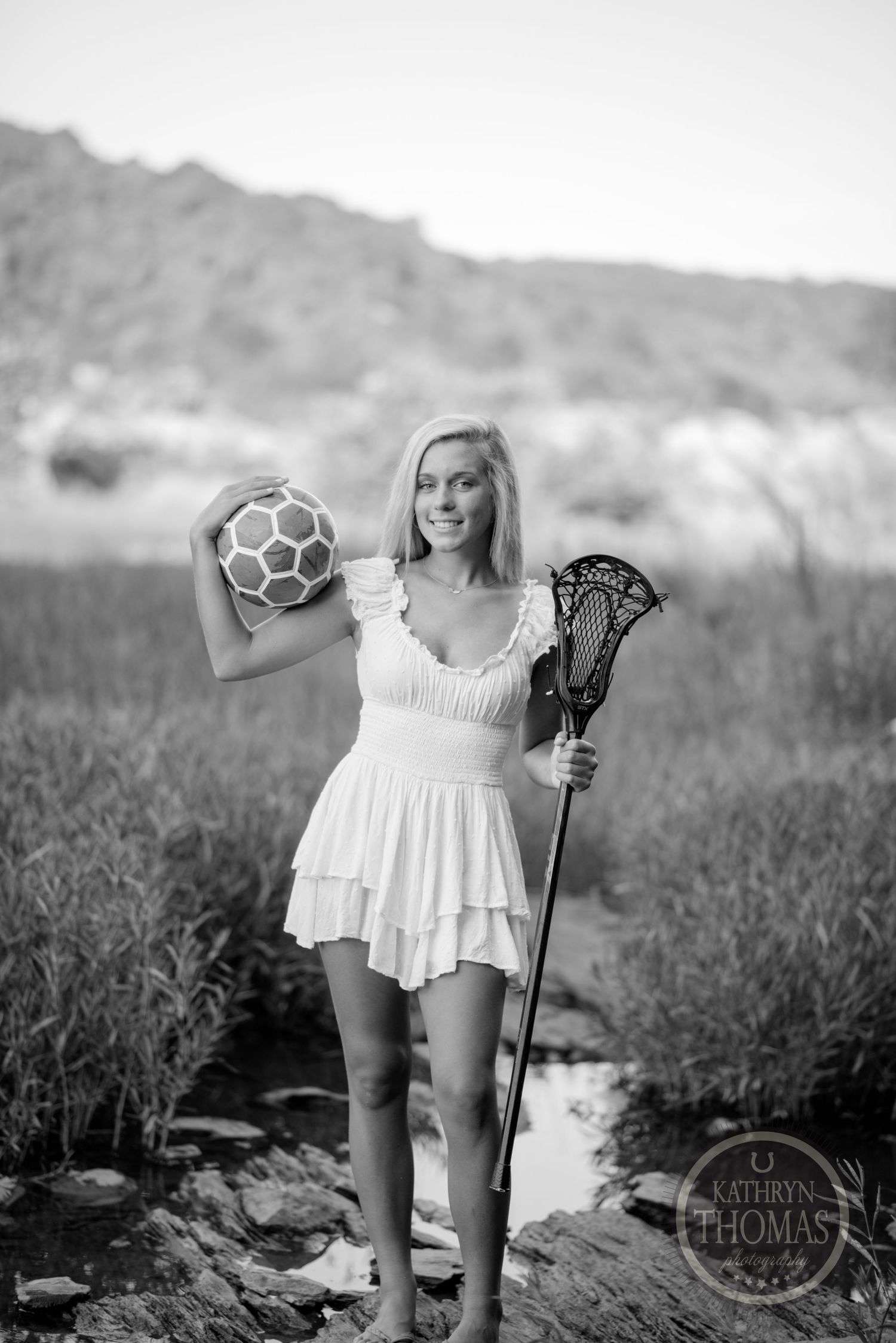 Athletic portrait with soccer ball and lacrosse stick in black and white outdoor setting.