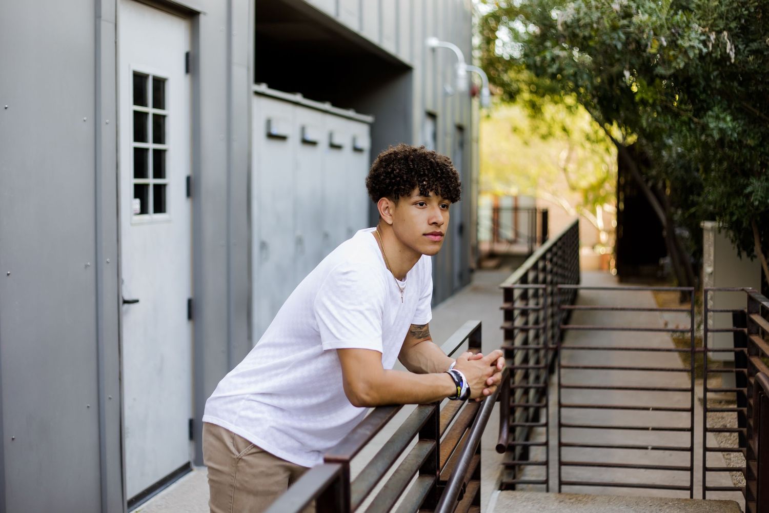 Senior boy poses leaning over the rail in an industrial location for his graduation senior portrait session.