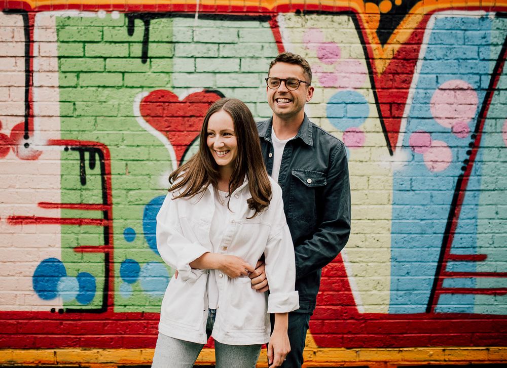 Couple posing against colorful graffiti wall with vibrant street art designs. Worcestershire Wedding photographer.