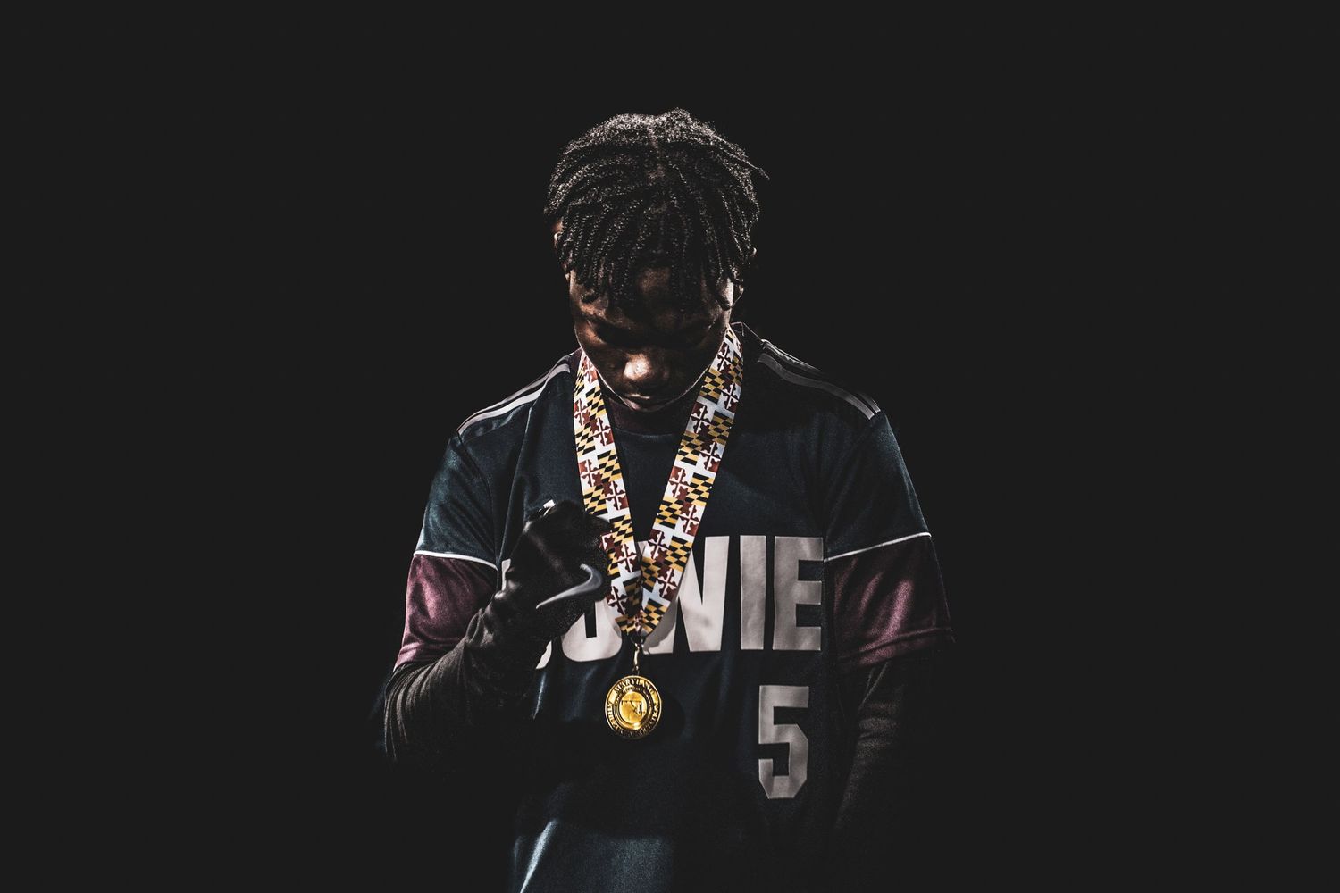 Soccer athlete wearing champtionship chain necklace and black jerset with number 5, posing against dark background.
