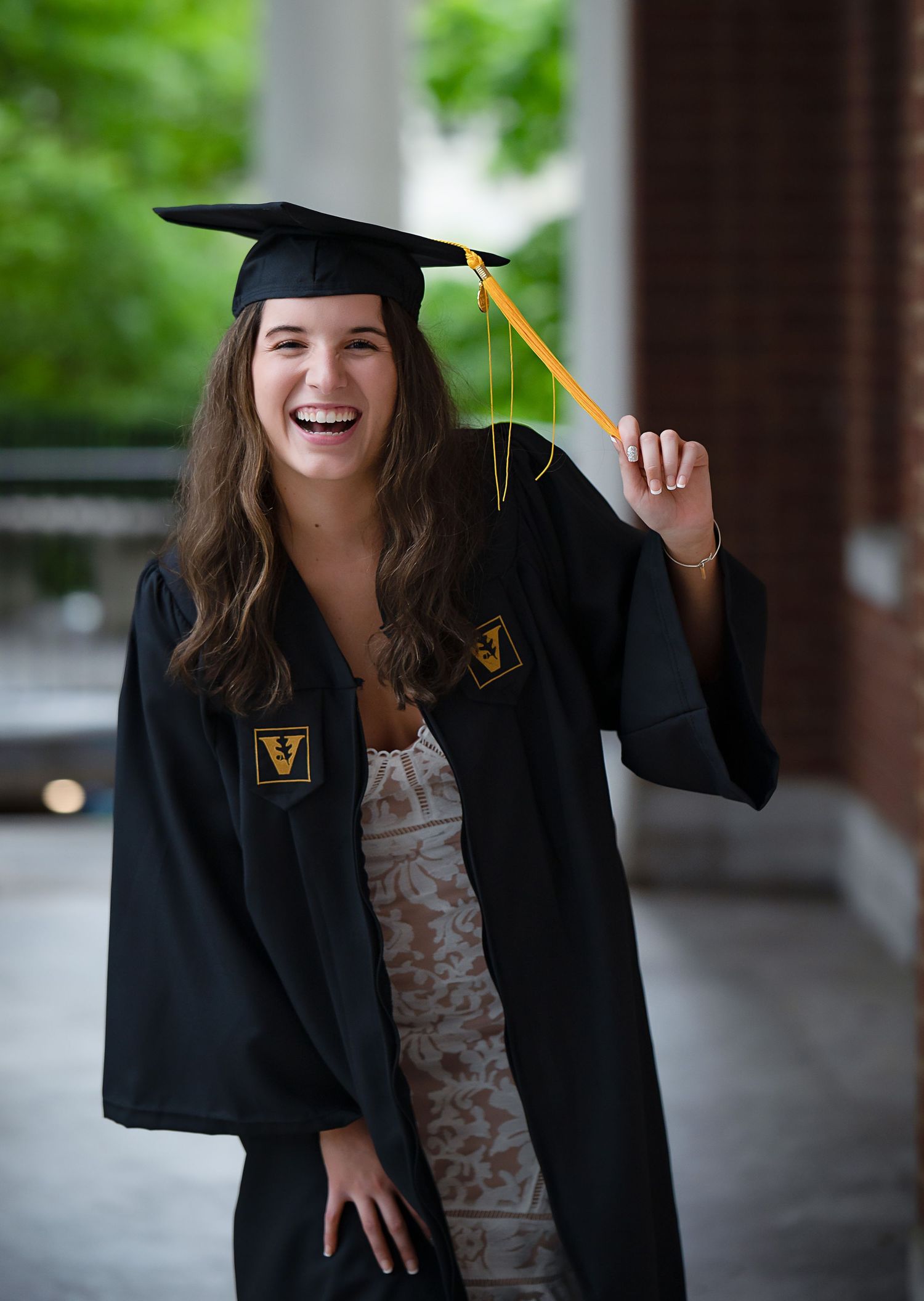Graduate in black cap and gown smiling joyfully on campus.
