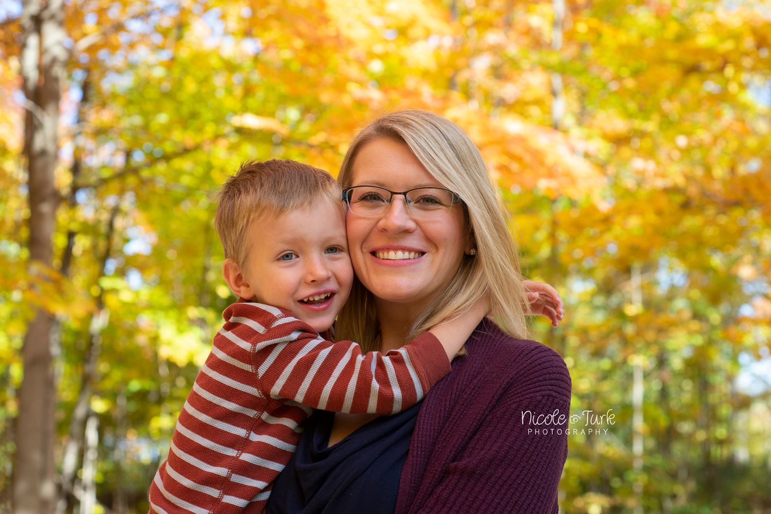 Mom and young son snuggle into each other for a close up photo in the fall leaves in Courtice
