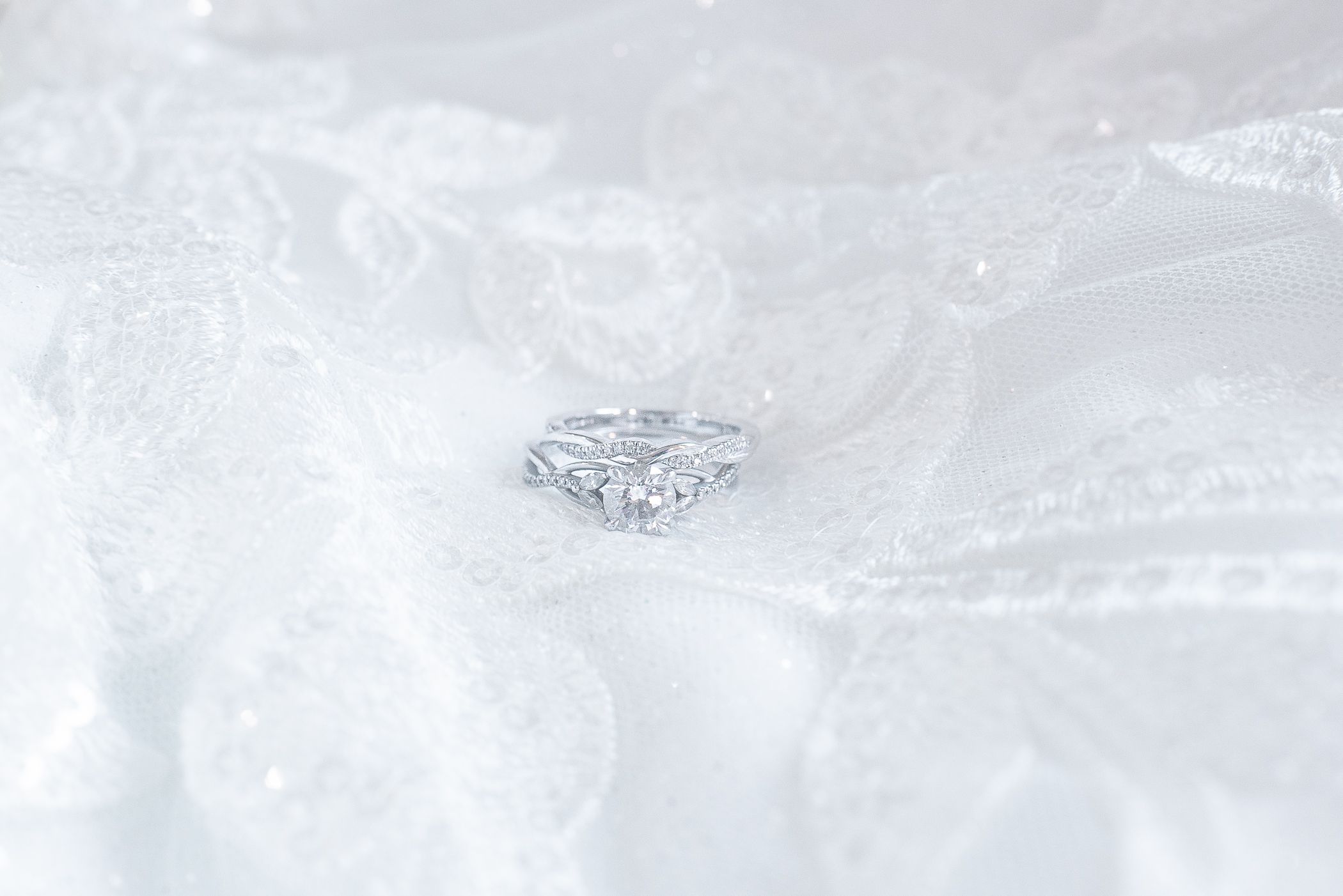 Diamond engagement ring nestled in white lace wedding dress fabric.