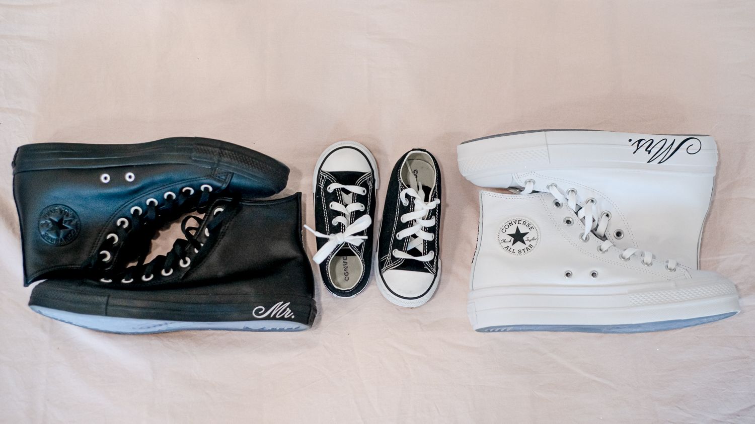 Three pairs of Converse sneakers in black, blue and white arranged on light background.