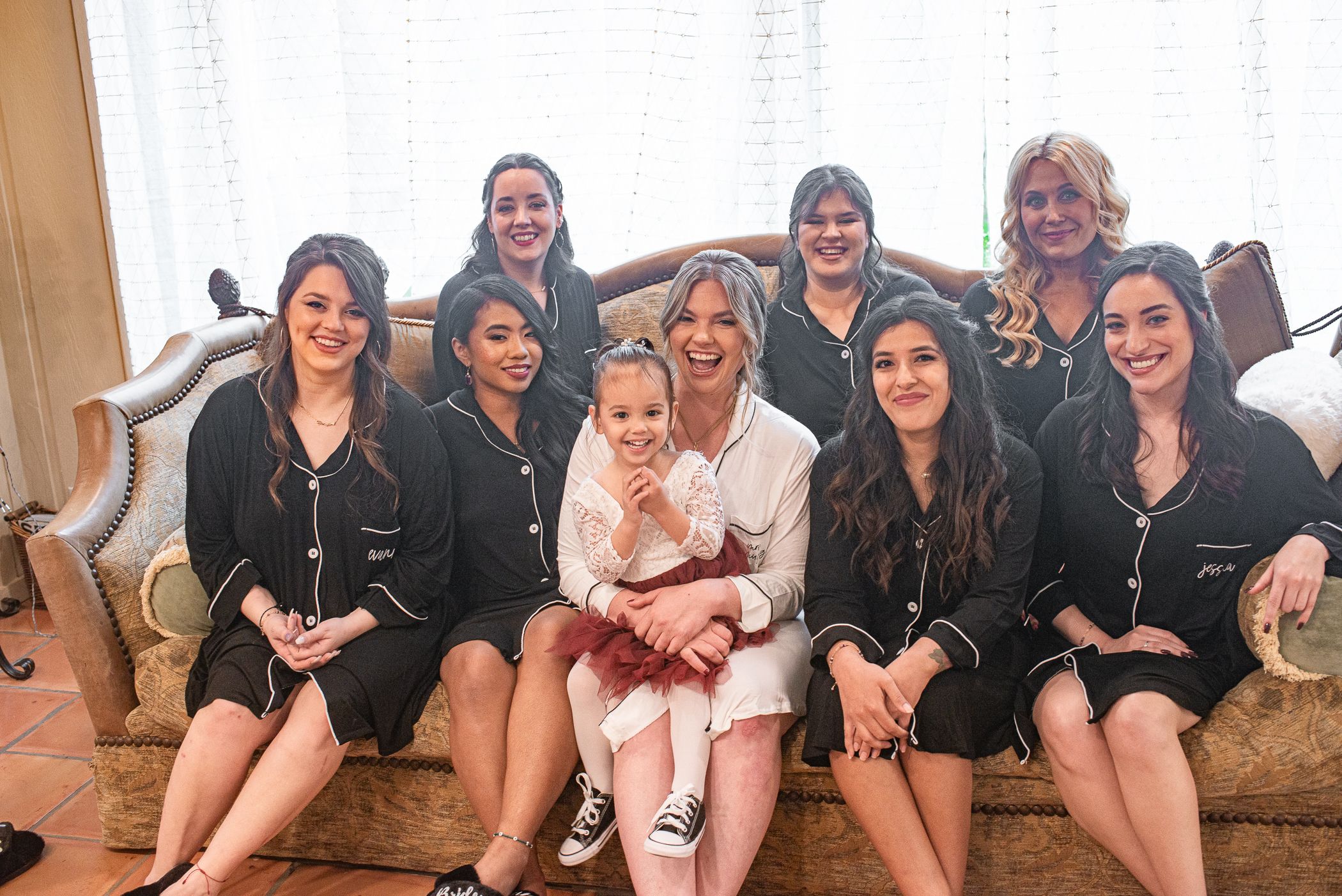 Wedding party in matching black robes sitting together on vintage brown couch.