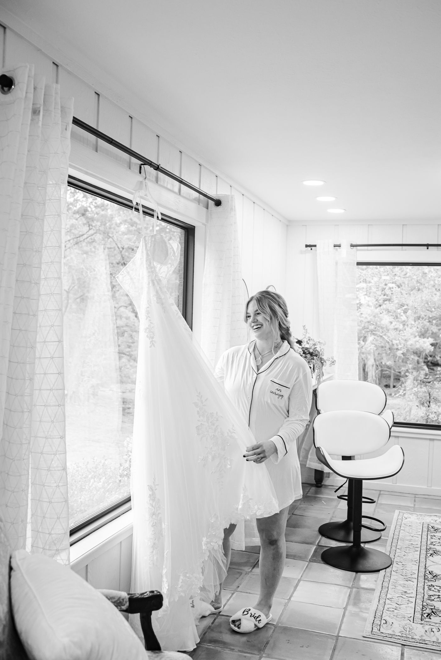 A wedding dress being prepared in a bright, modern dressing room with large windows.