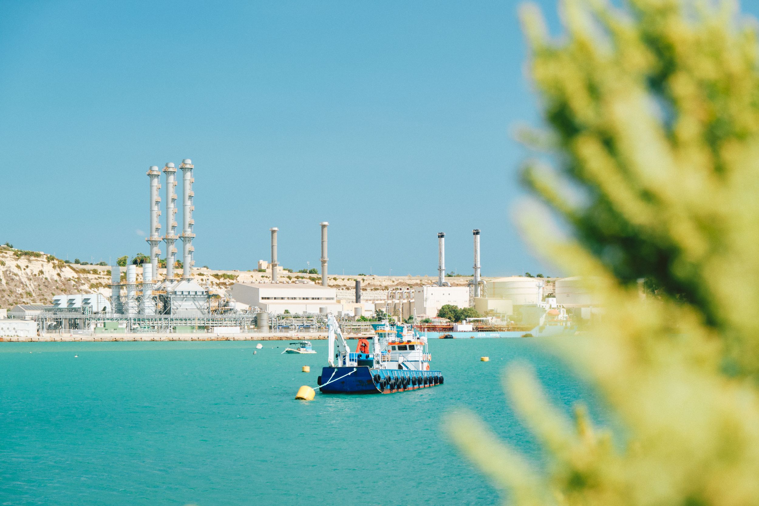 Industrial port with smokestacks and blue cargo ship in crystal clear turquoise waters.