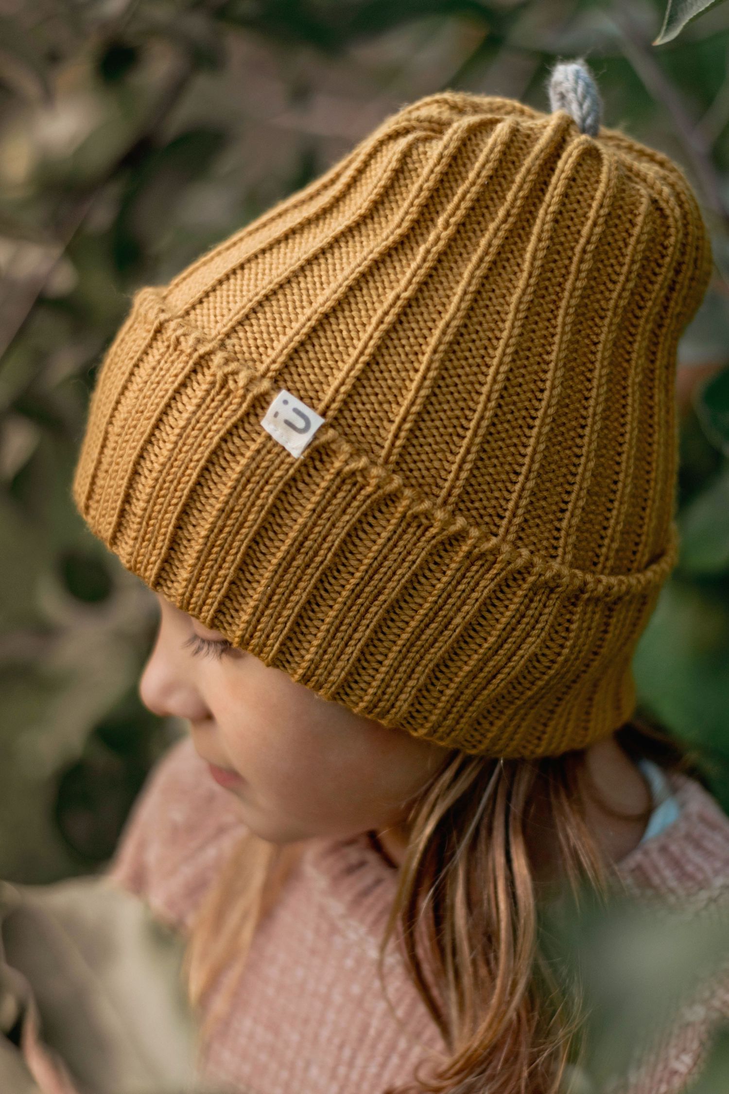 Close-up of a brown knit beanie with ribbed texture against a blurred natural background.