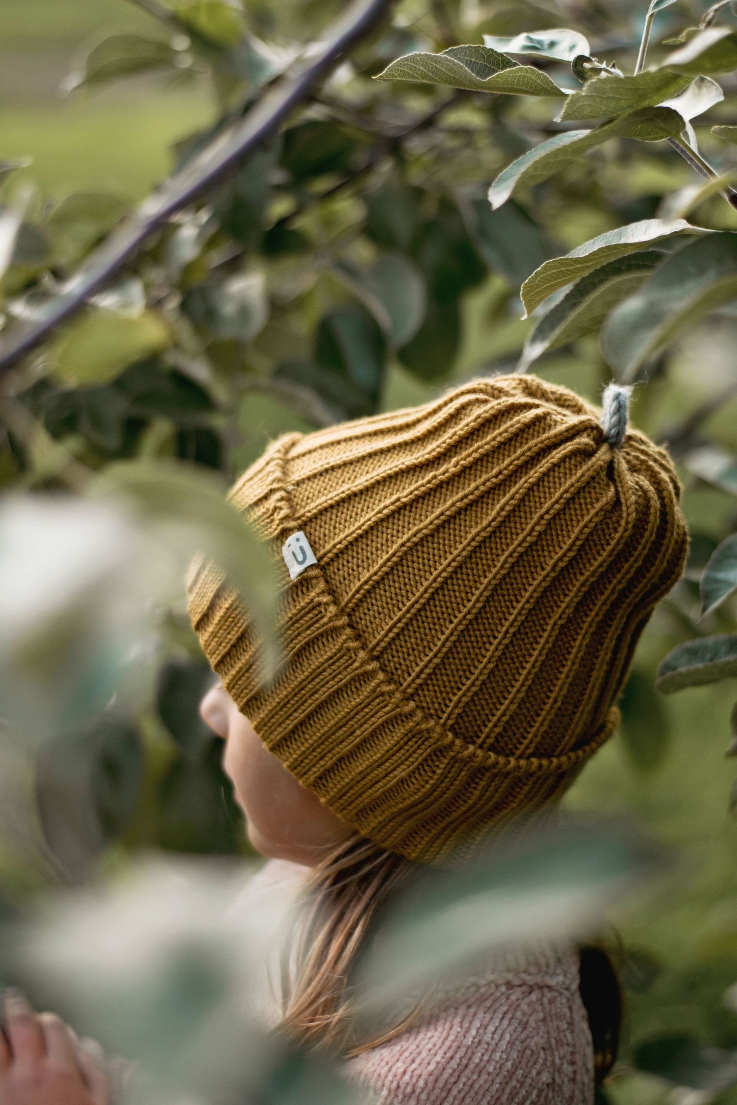 Side view of a mustard yellow knit beanie with ribbed pattern among green leaves.