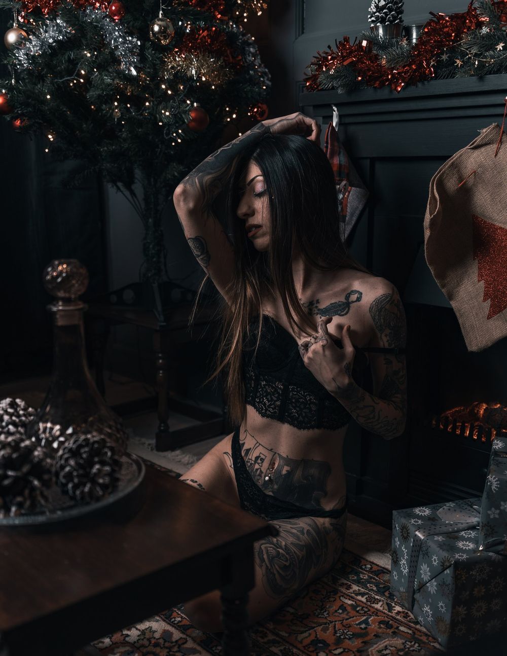 Artistic portrait of tattooed figure in lingerie against holiday decor with dramatic lighting.