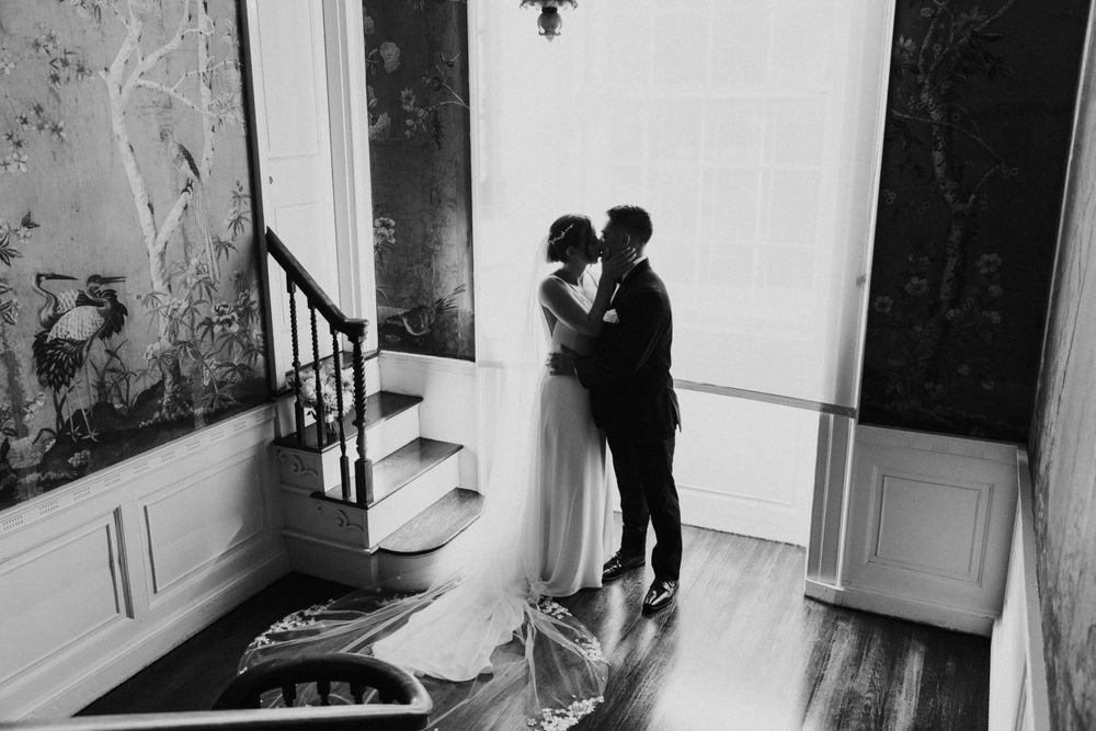 Black and white photograph of a romantic moment in an elegant hallway with natural light.