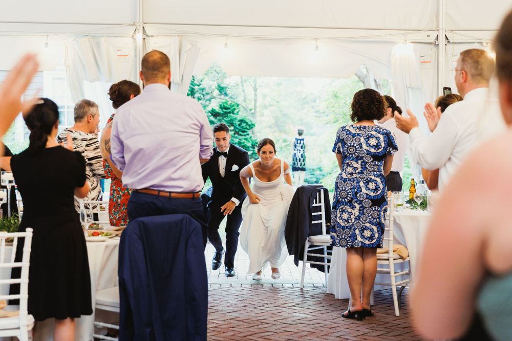 Wedding celebration in a white tent with guests gathered around tables.