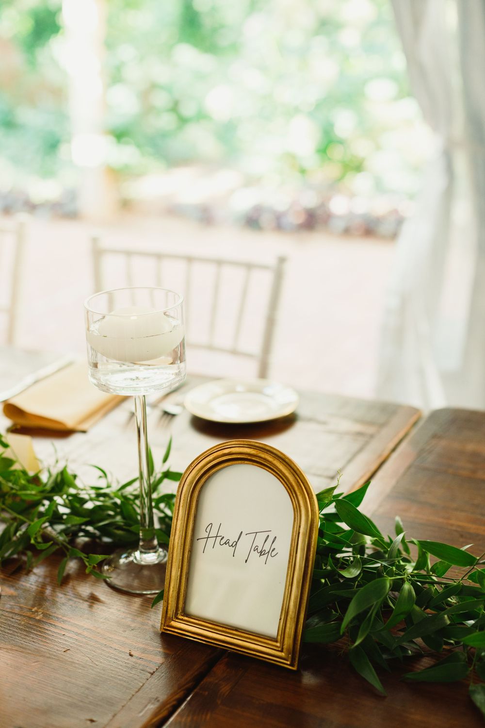 Wedding reception table setting with gold framed head table sign and greenery garland decor.