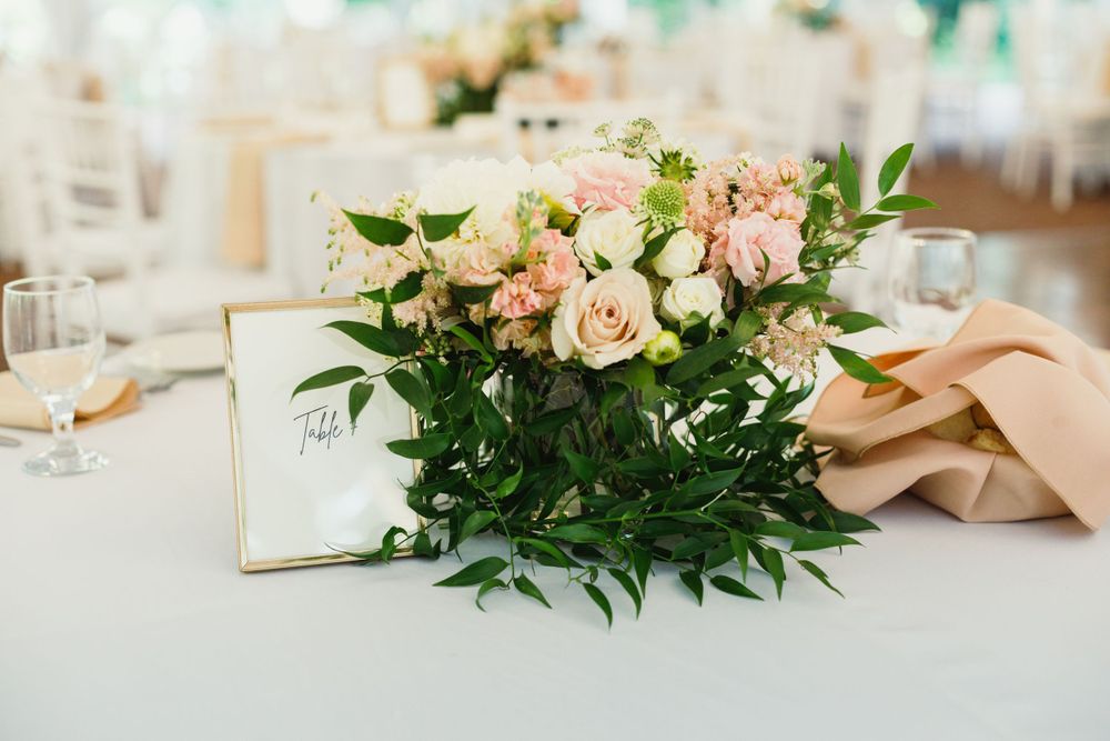 Romantic table centerpiece with blush roses and greenery next to gold framed signage.