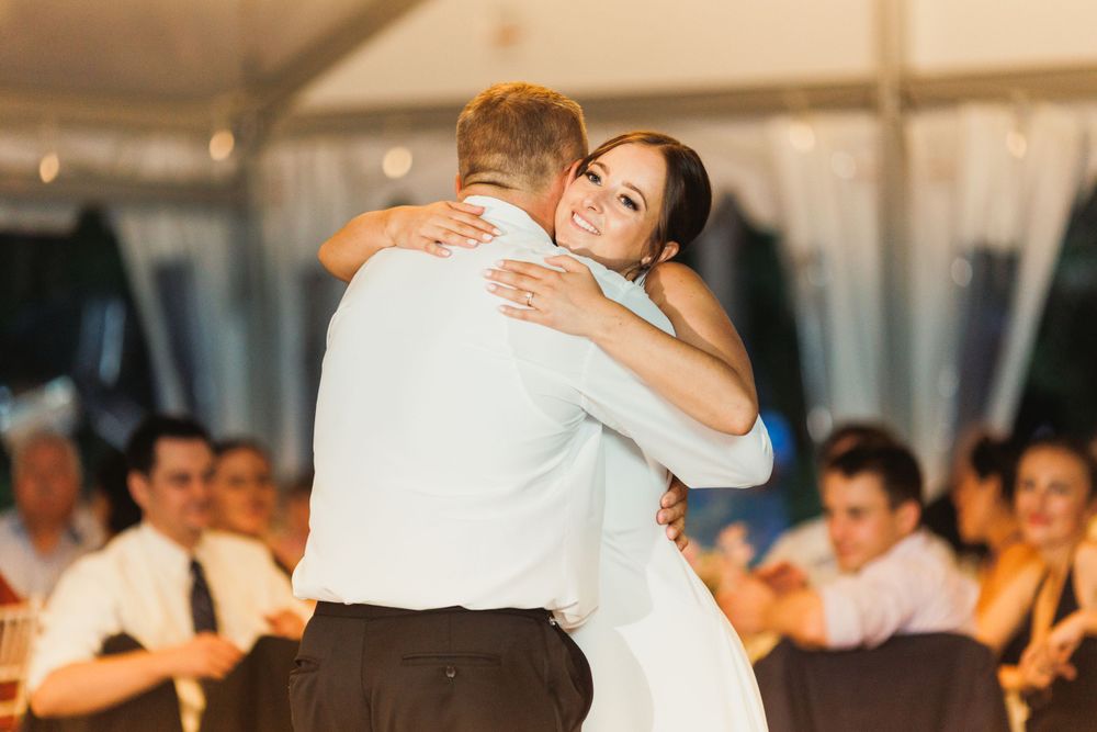 Bride and father share emotional dance moment at wedding reception while guests look on.