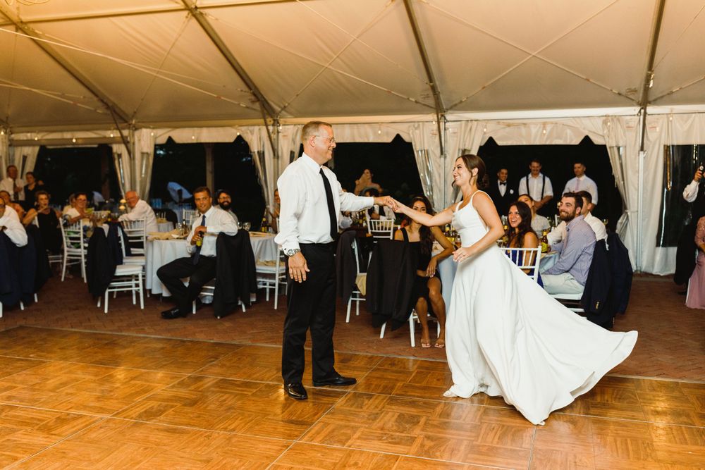 Couple performs playful dance move on wooden floor during wedding reception.