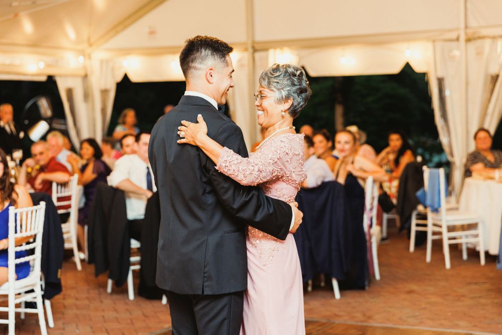 Couple dances together at wedding reception while guests watch from decorated tables in background.