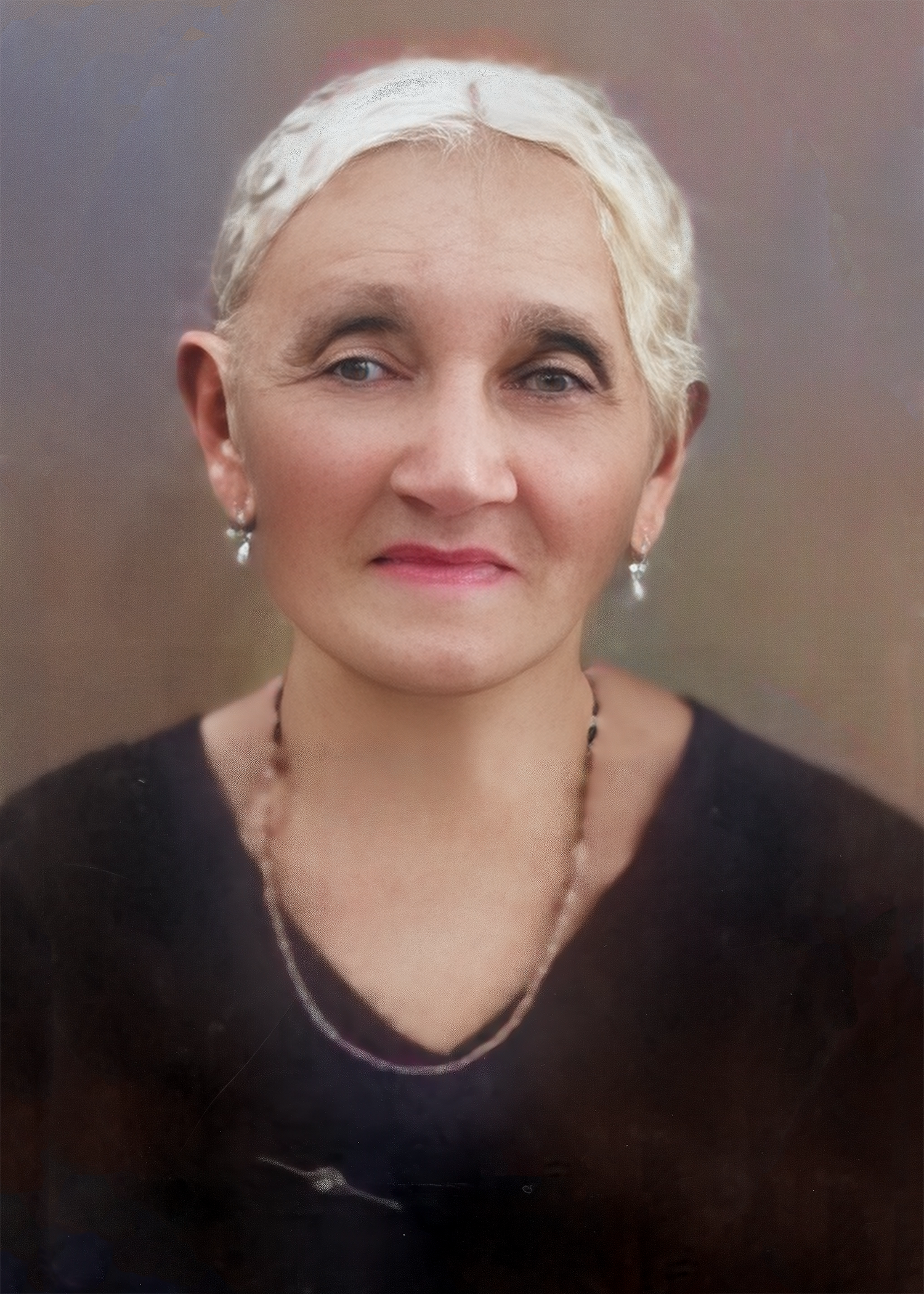 Portrait of a person with white hair wearing a black top and necklace, with a warm genuine smile.