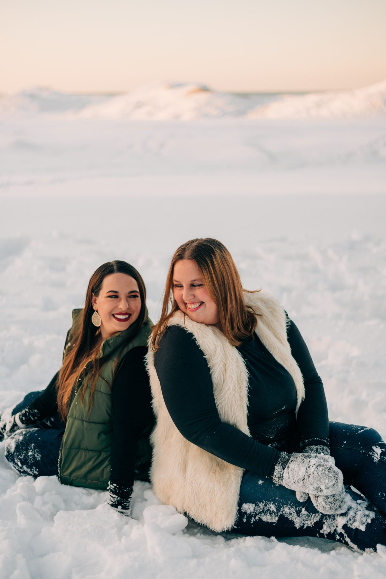 photo of two sisters sitting in the snow on a snowy beach at sunset